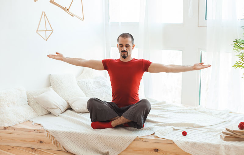 ベッドの上であぐらを組み両腕を大きく広げている男性