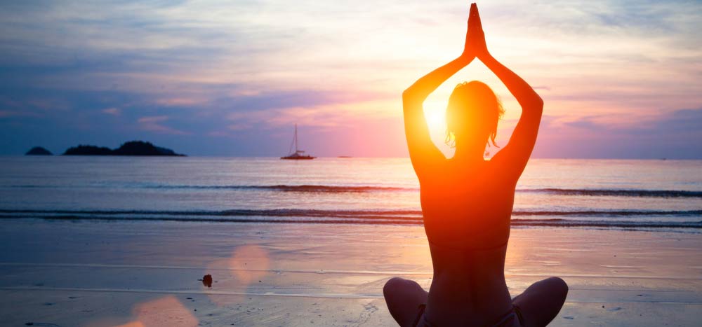 海辺で頭の上で合掌する女性のシルエット