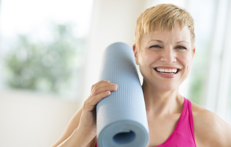笑顔で丸めたヨガマットを肩に乗せる女性