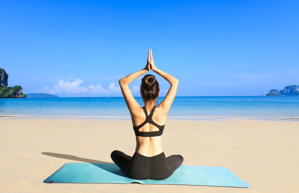 ビーチでヨガマットを敷き海に向かってヨガポーズをとる女性