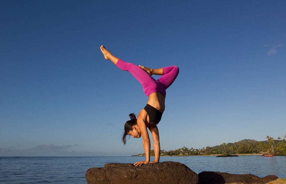 ヨーコ・フジワラが岩の上でハンドスタンドをしている様子