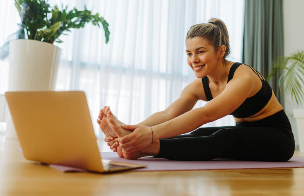 パソコンの画面を見ながらヨガをする女性