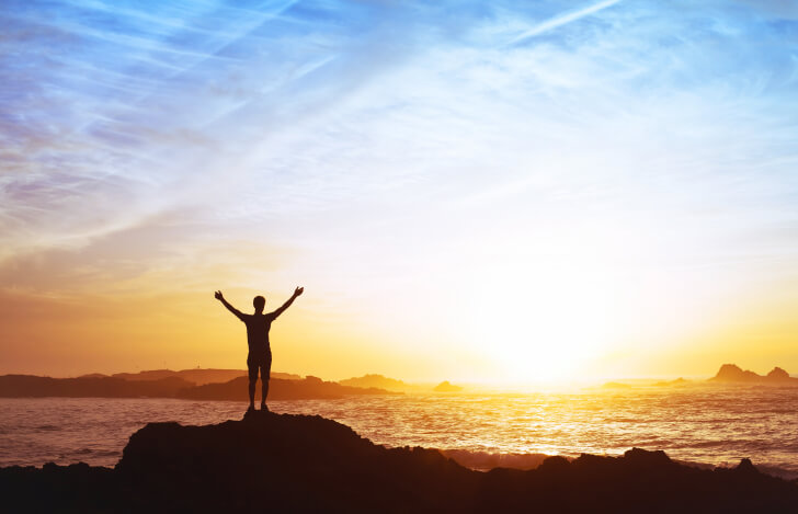 海に沈む夕焼けに両手を挙げる人のシルエット