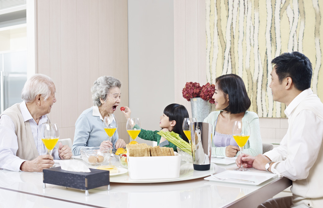 家族3世代が食卓を囲んでいる。おばあちゃんの口に食べ物を運ぶ女の子の孫