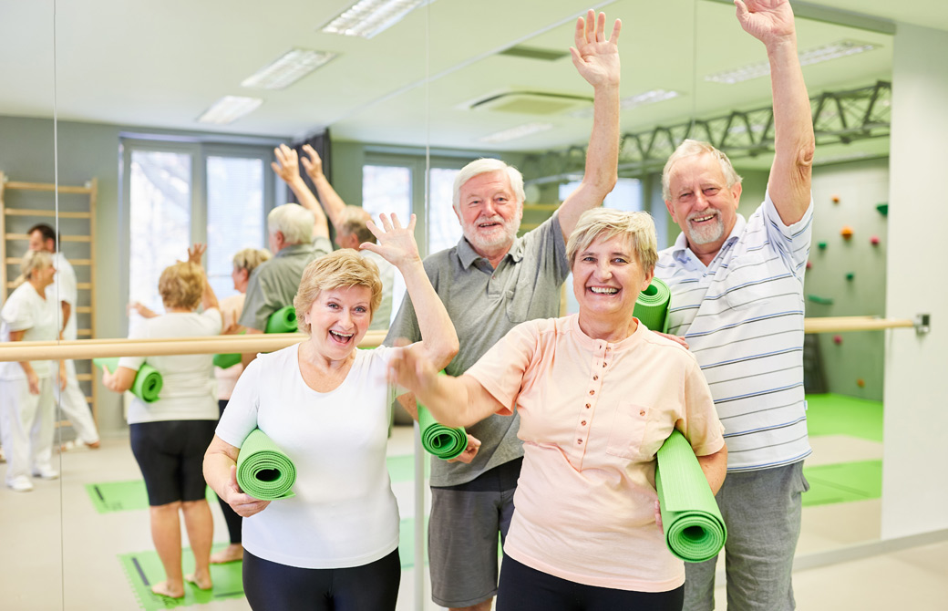 スポーツクラブでヨガマットを持って手を振る老人の男女