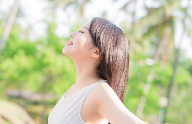 自然の中で目を閉じ笑顔で深呼吸する女性