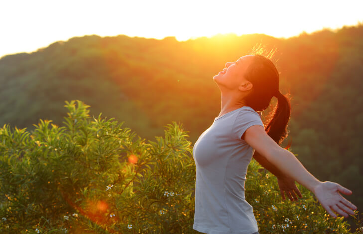 自然の中で両手を広げて深呼吸する女性