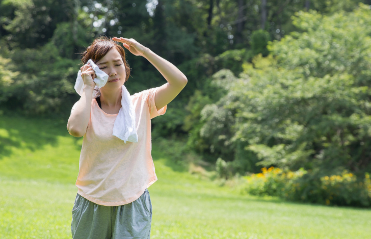 汗を拭きながら外を歩く女性