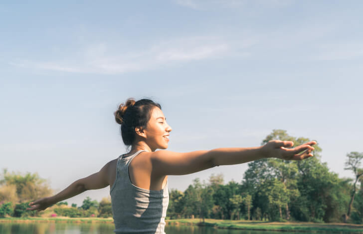 青空の下で気持ちよさそうに両手を広げた女性