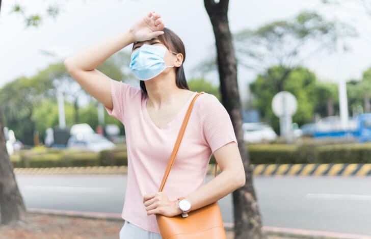 熱中症で額に手を当てるマスク姿の女性