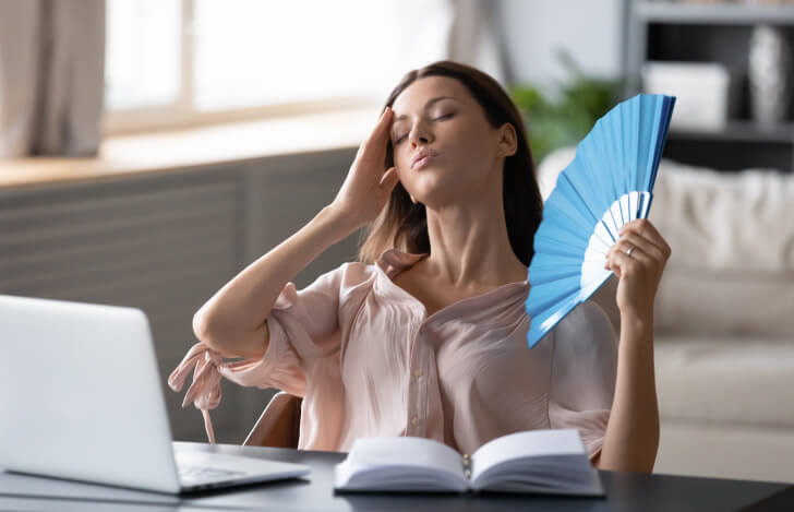 パソコンに向かいながら扇子で仰ぐ疲れた女性