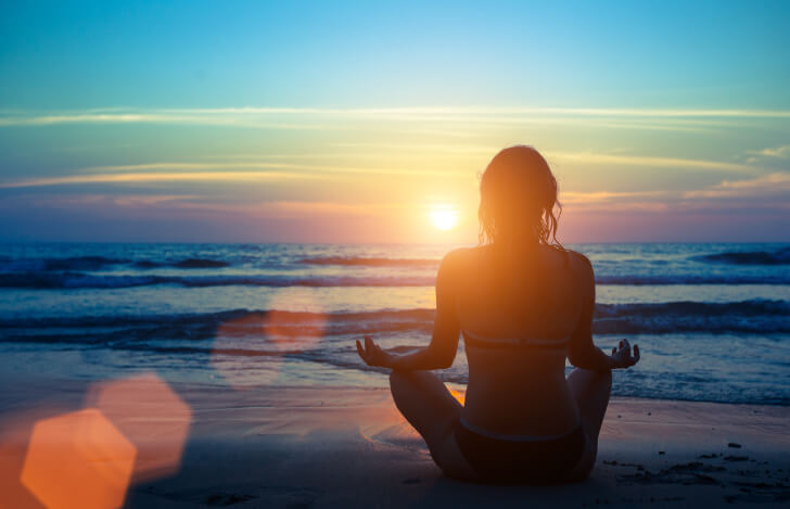 砂浜で夕焼けを眺める女性の後ろ姿