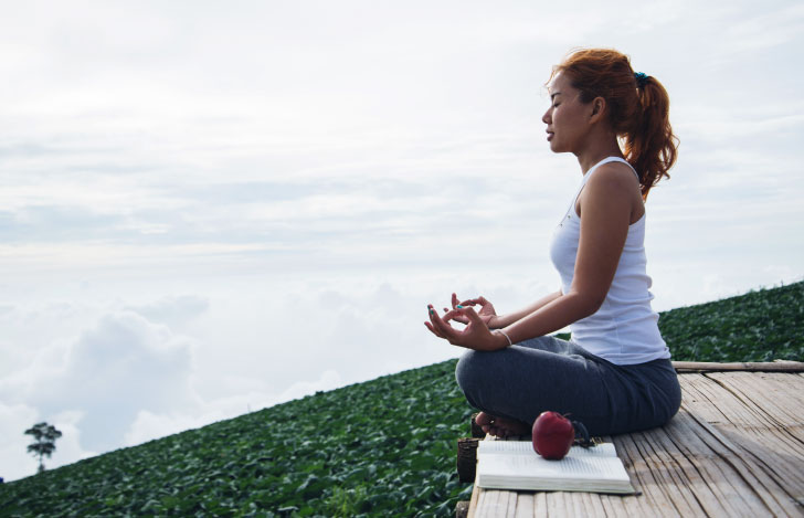 ヨガの本を傍に瞑想する女性