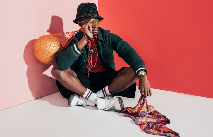 アスレジャーファッションに身を包み赤い壁の前に座る一人の男性