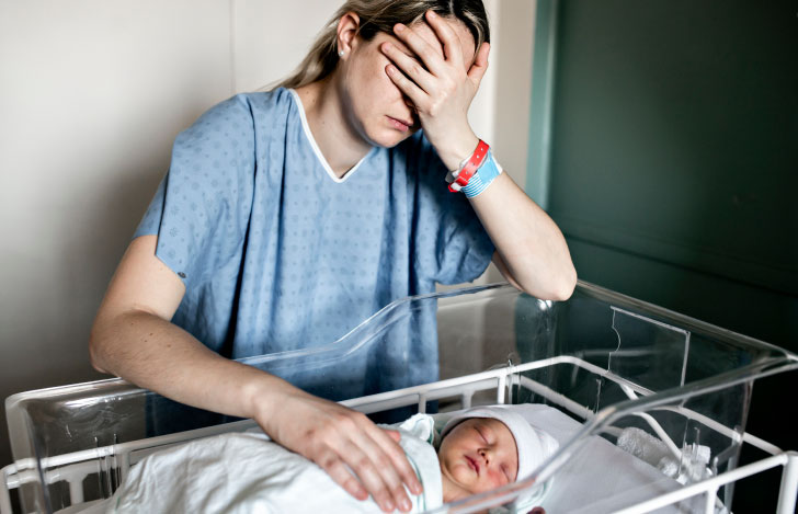 新生児ベッドの横で辛そうに手で顔を覆う女性