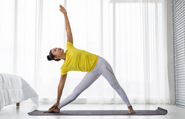 室内でヨガを行う黄色いTシャツ姿の女性