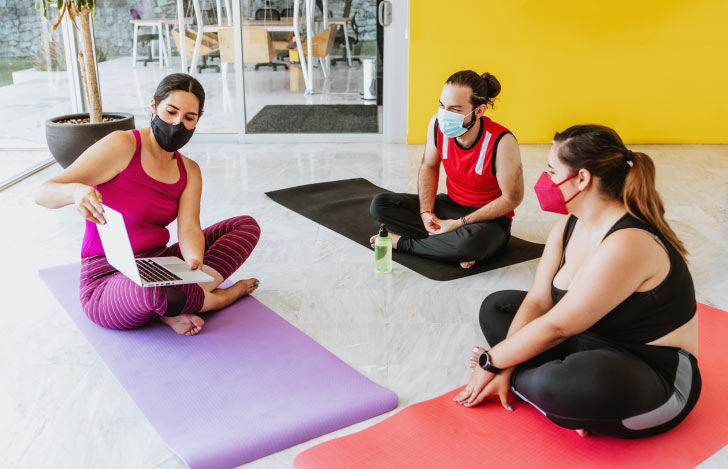 マットの上でノートPCを手にし、マスクを付けたた女性から説明を受けるマスク姿の男女