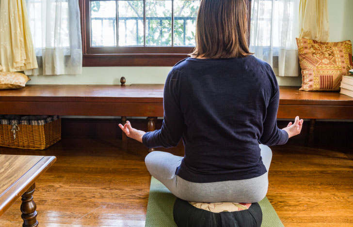 ヨガマットの上のクッションに座って瞑想する女性