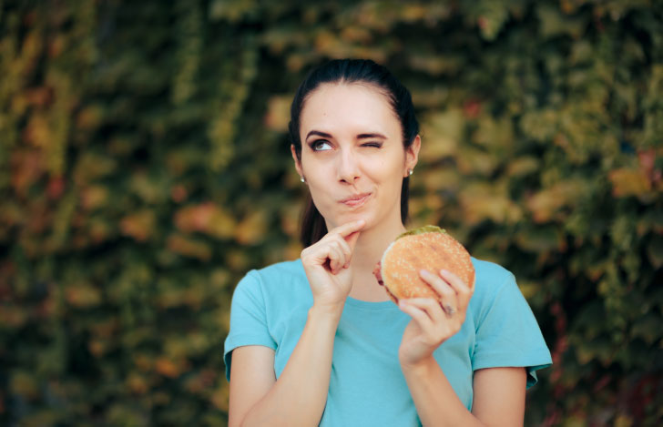 ハンバーガーを手に食べることを悩んでいる女性
