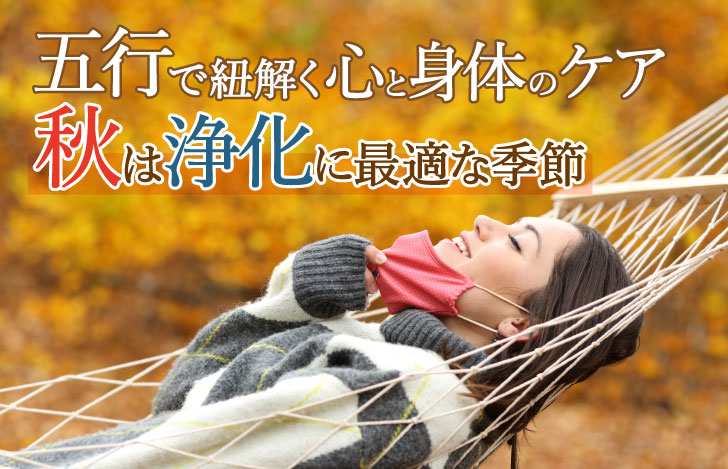 紅葉の木々の中でハンモックに横たわり口元からマスクを外す女性