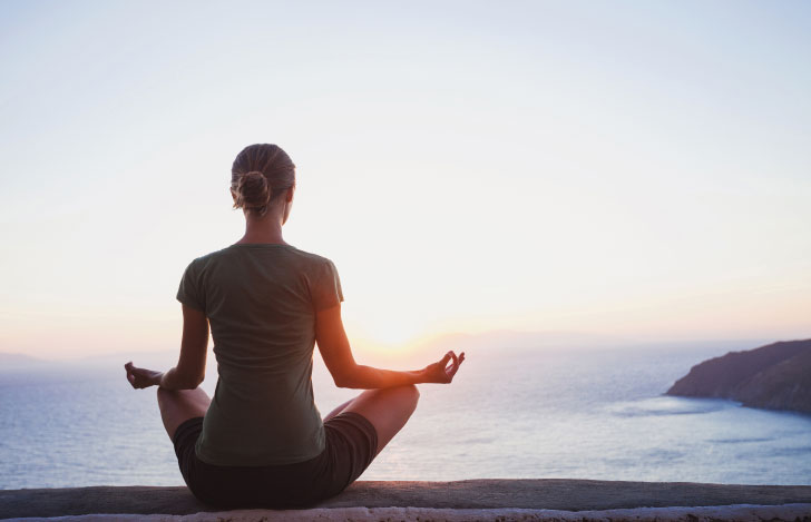 海岸で安楽座で座る女性の後ろ姿