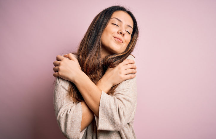 自分自身をハグしながら嬉しそうな表情を浮かべる女性