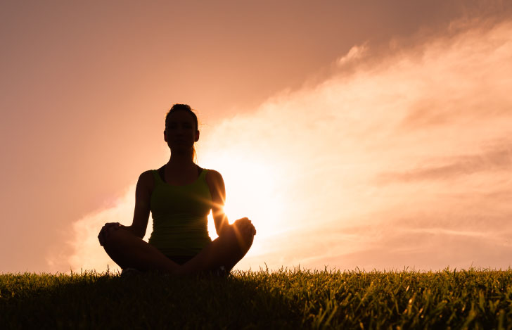 夕日を背に瞑想する人のシルエット