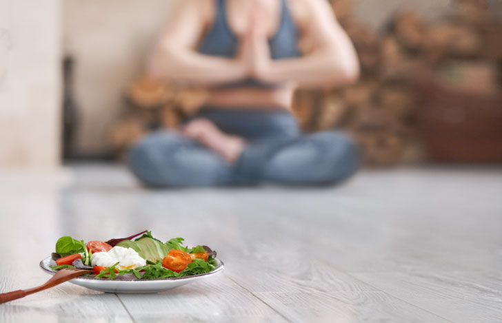 食べ物がのった皿の向こうでヨガをする女性