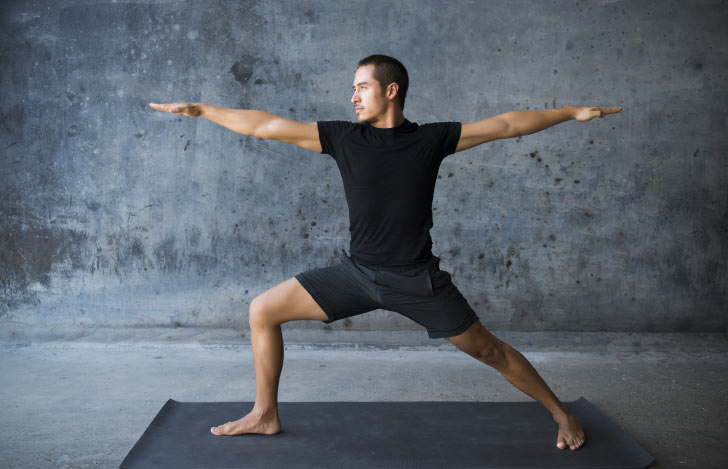 戦士のポーズ2をとるグレーのヨガウェアを着た男性