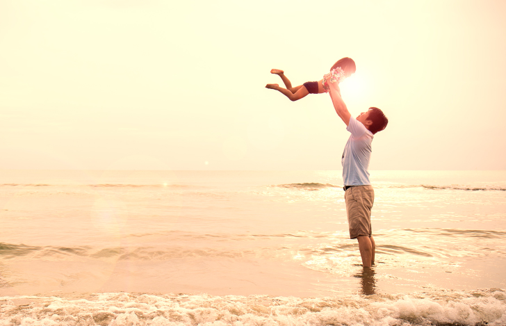 海辺で小さい女の子を抱き上げる父親