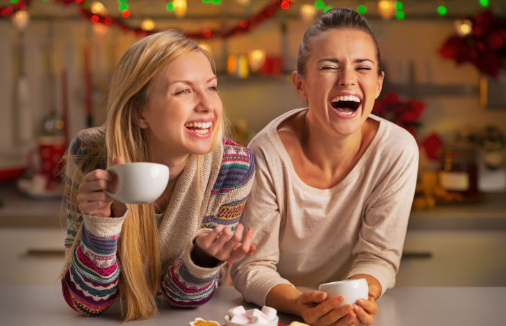 カップを手に床でくつろぎ談笑する二人の女性