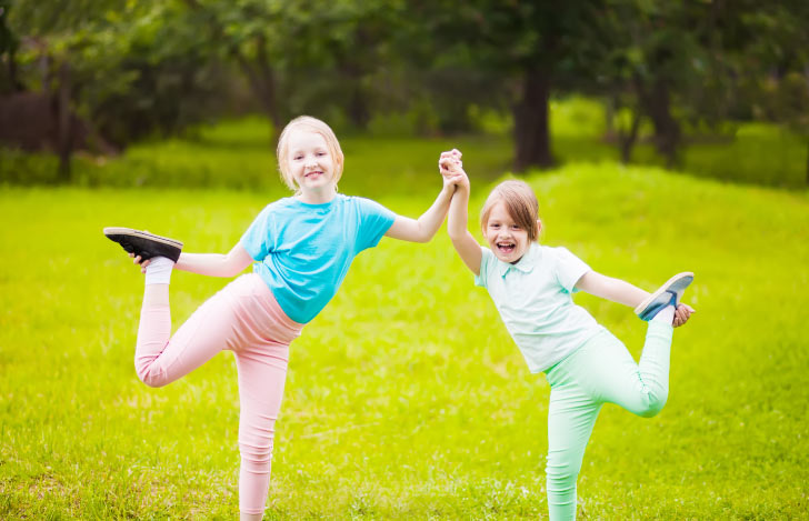 原っぱでヨガのような動きを楽しむ二人の子供