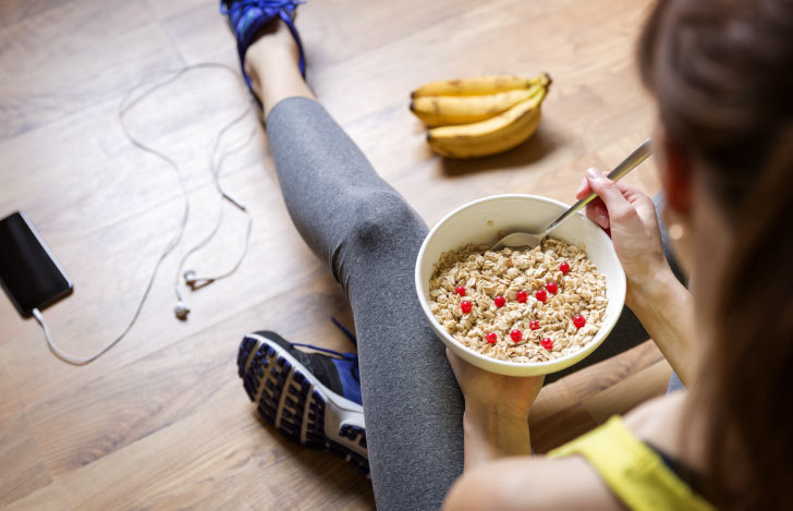 スプーンを手に果物とオートミールが入ったボウルを足元に乗せている女性