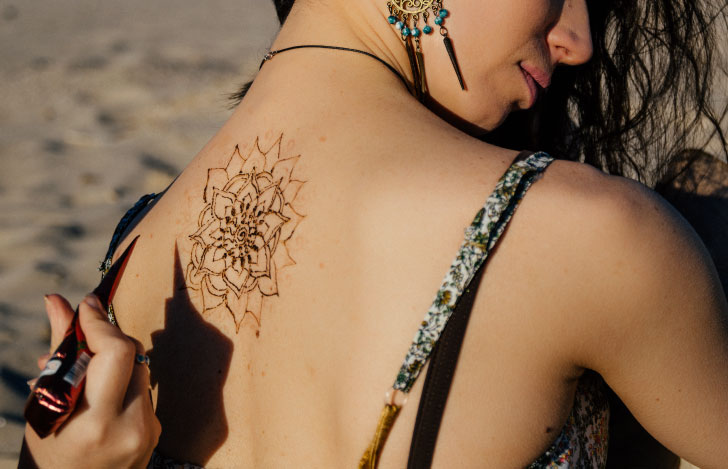 ヘナアーティストが女性の背中にヘナを施しているところ