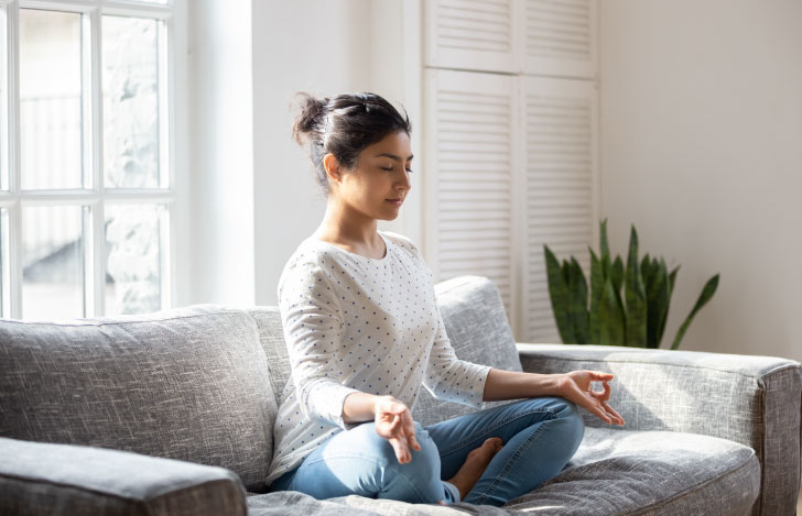 ソファの上で穏やかな表情で呼吸法を行う女性