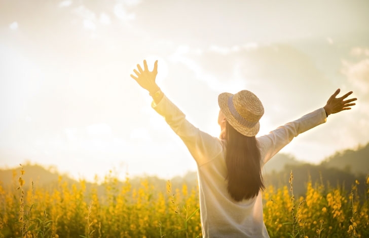 花畑で両手を広げて空を見上げる女性