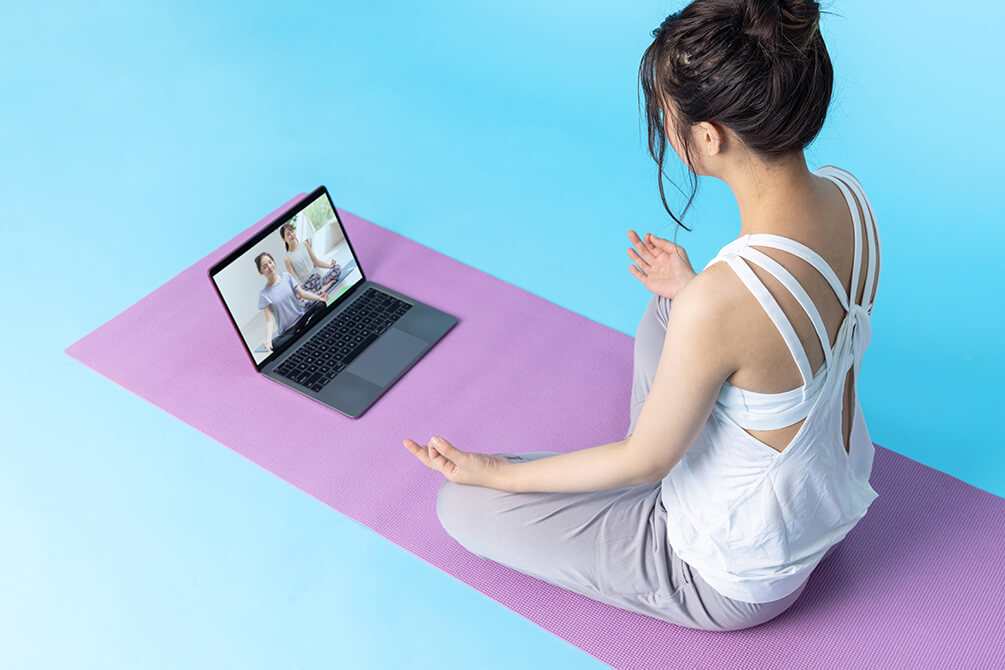 ヨガマットの上でオンラインヨガを受ける女性