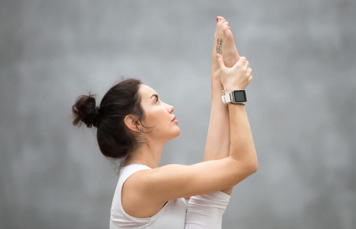 ヨガの足を持ち上げるポーズをする女性