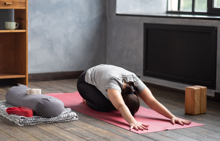 室内のヨガマットの上でチャイルドポーズをする女性
