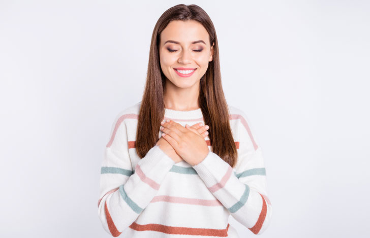 両手を胸に当て笑顔で目を閉じる女性