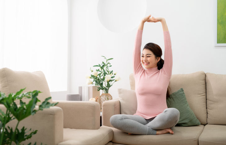 室内のソファの上で伸びをする笑顔の女性