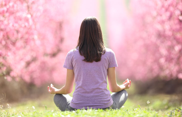 満開の桜の木々に囲まれてヨガを行う女性の背中