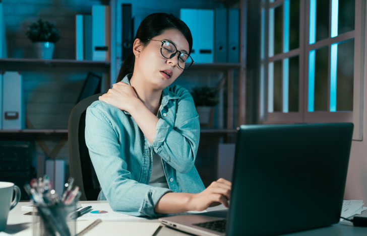 夜にPCの前で肩に手を当てた疲れた女性