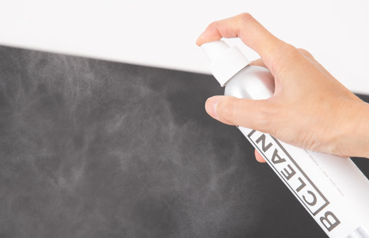 ヨガマットにクリーナースプレーを吹き付ける人の手もと