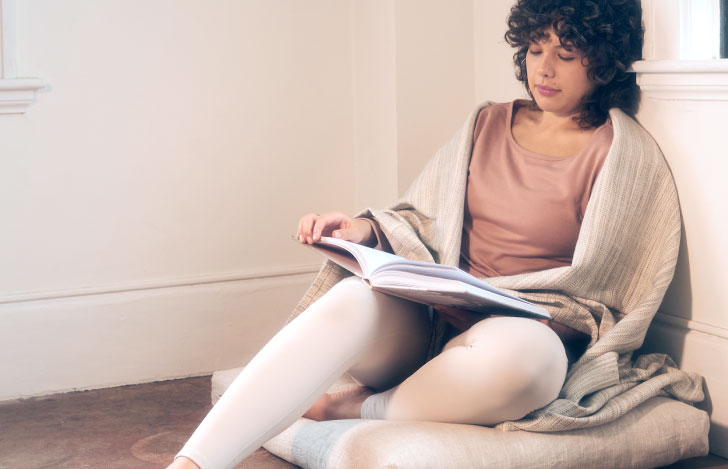 ヨガブランケットをまとって雑誌を読みながらくつろぐ女性