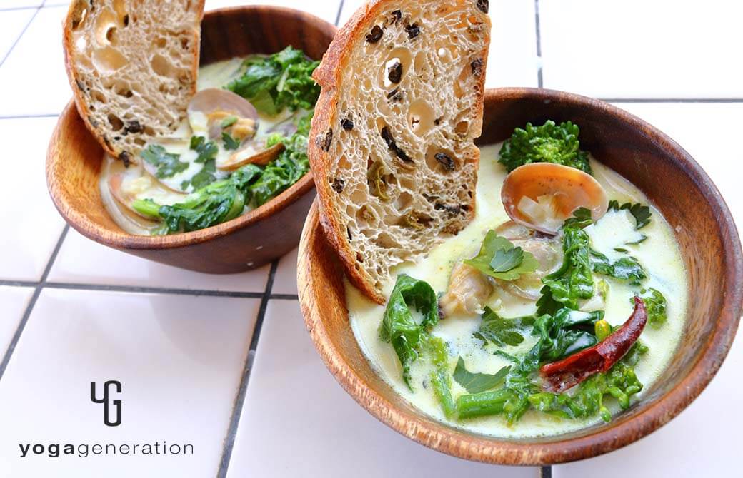 木の器に盛り付けた菜の花とアサリのスパイシーなミルクスープ