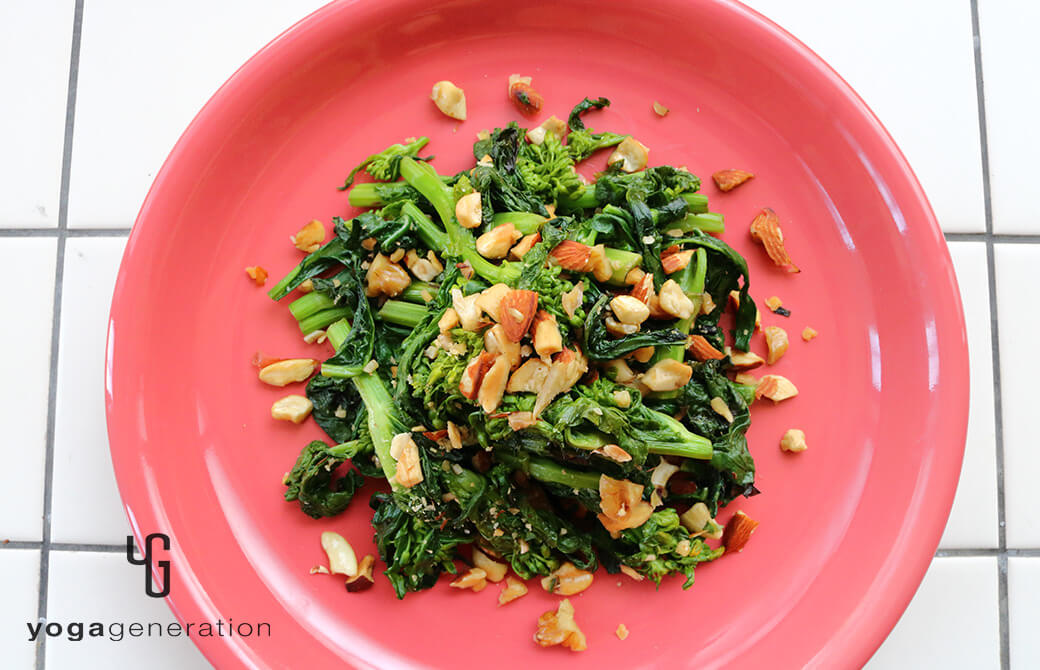 黄みがかったピンクのお皿に盛り付けた菜の花と色々ナッツの塩炒め