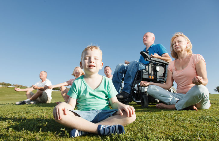 芝生の上でヨガをする男児と年配の女性と車椅子の年配の男性たち