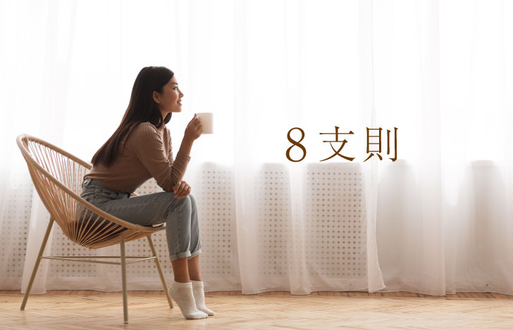 窓辺でマグカップを手に椅子に座る女性の姿