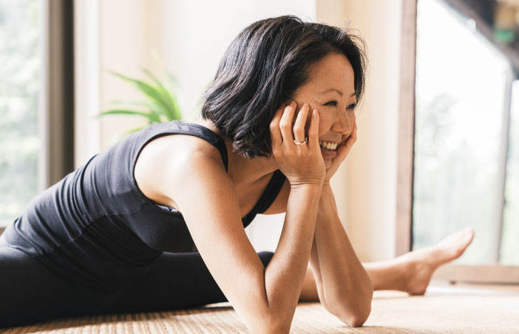 開脚をしながら床に肘をついて頬杖する笑顔の女性